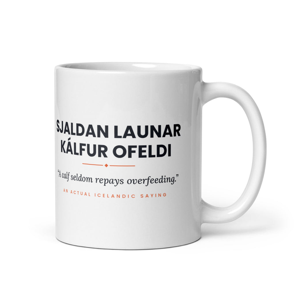 White 11 oz Sjaldan launar kálfur ofeldi mug, handle on the right, showing black lettering, English translation and coral accents.
