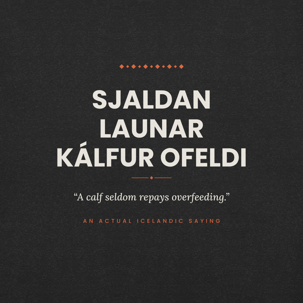 Close-up of the Sjaldan launar kálfur ofeldi front print, showing cream lettering, English translation and coral accents on Black Heather fabric.