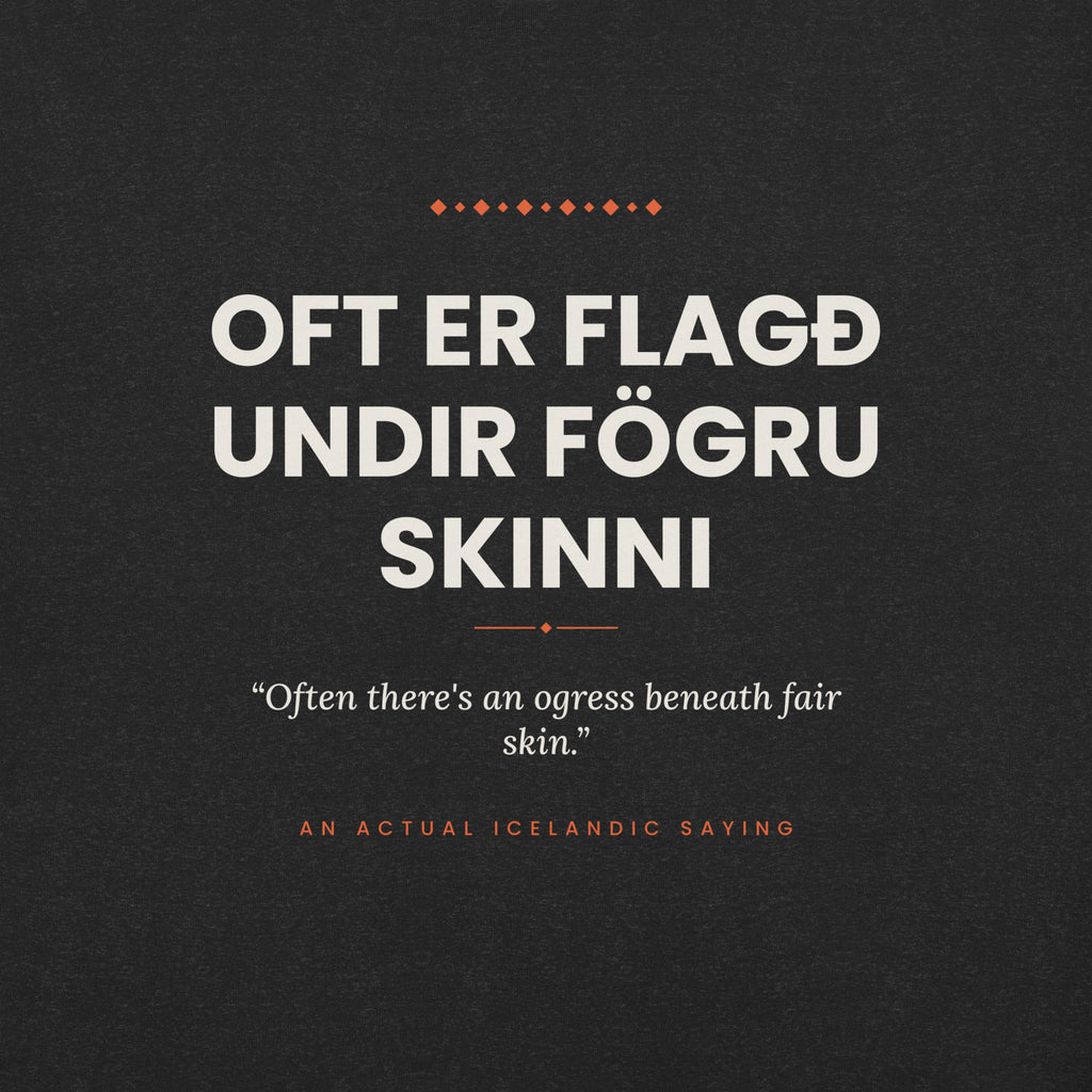 Close-up of the Oft er flagð undir fögru skinni front print, showing cream lettering, English translation and coral accents on Black Heather fabric.