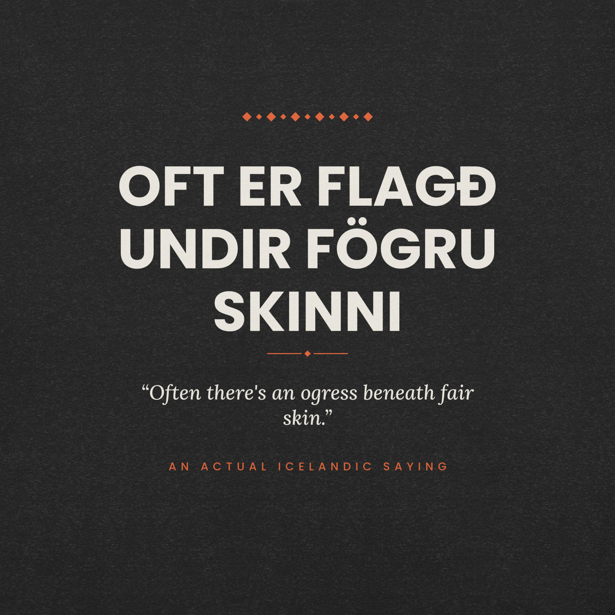 Close-up of the Oft er flagð undir fögru skinni front print, showing cream lettering, English translation and coral accents on Black Heather fabric.