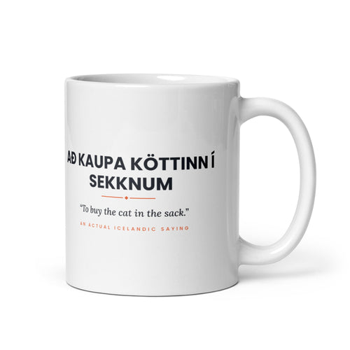 White 11 oz Að kaupa köttinn í sekknum mug, handle on the right, showing black lettering, English translation and coral accents.