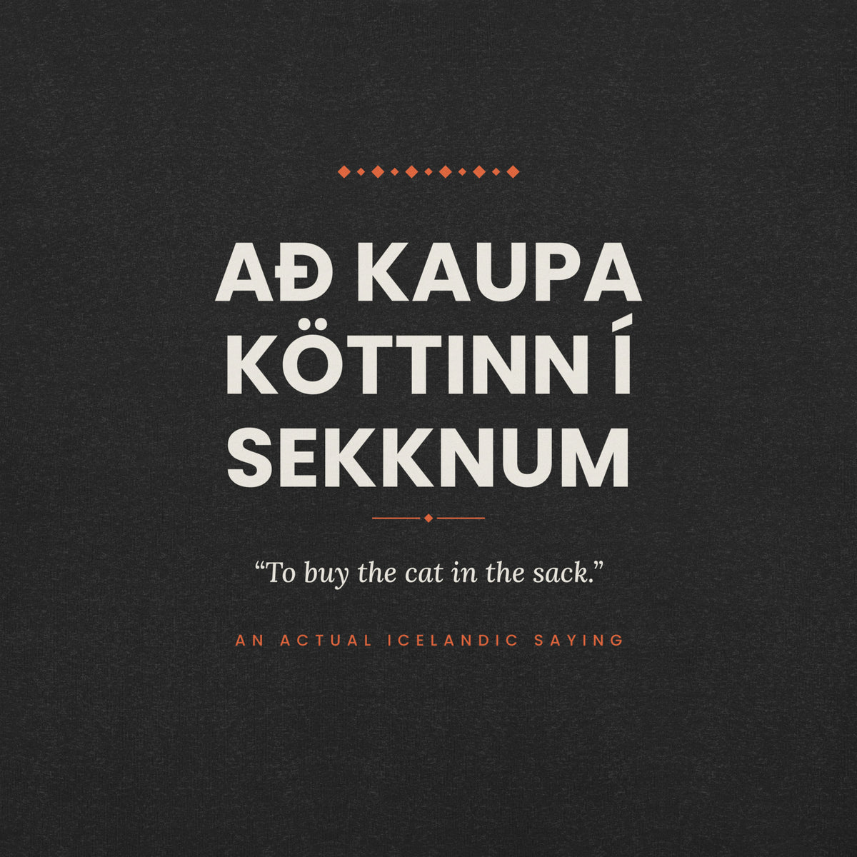 Close-up of the Að kaupa köttinn í sekknum front print, showing cream lettering, English translation and coral accents on Black Heather fabric.