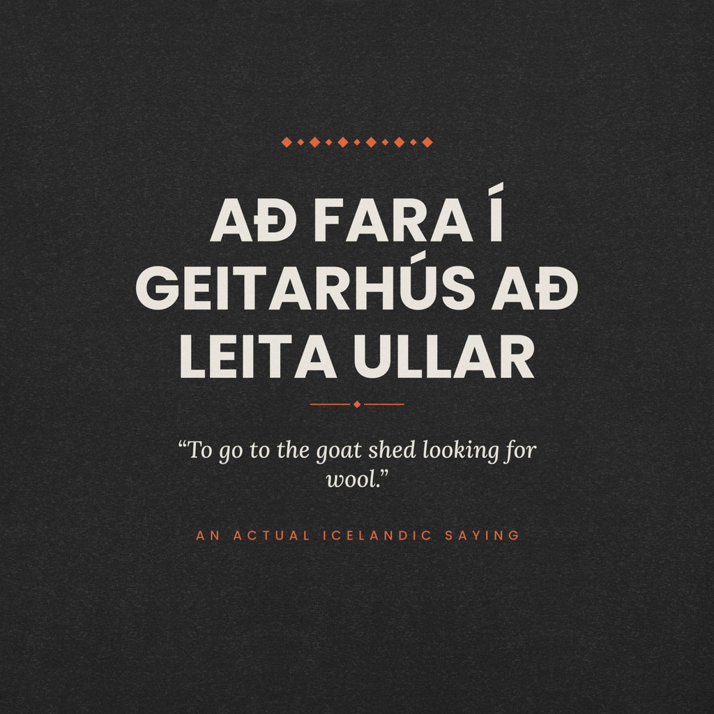 Close-up of the Að fara í geitarhús að leita ullar front print, showing cream lettering, English translation and coral accents on Black Heather fabric.