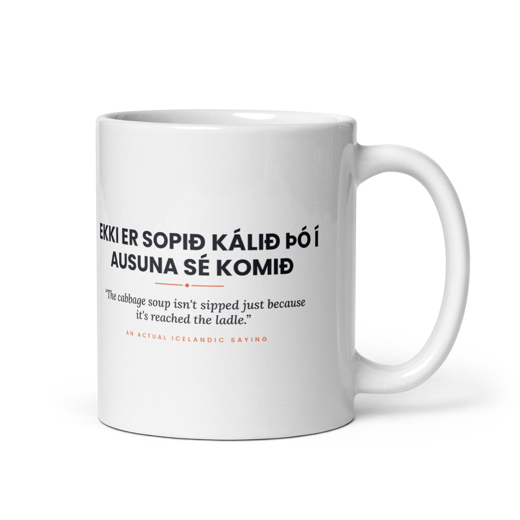 White 11 oz Ekki er sopið kálið þó í ausuna sé komið mug, handle on the right, showing black lettering, English translation and coral accents.