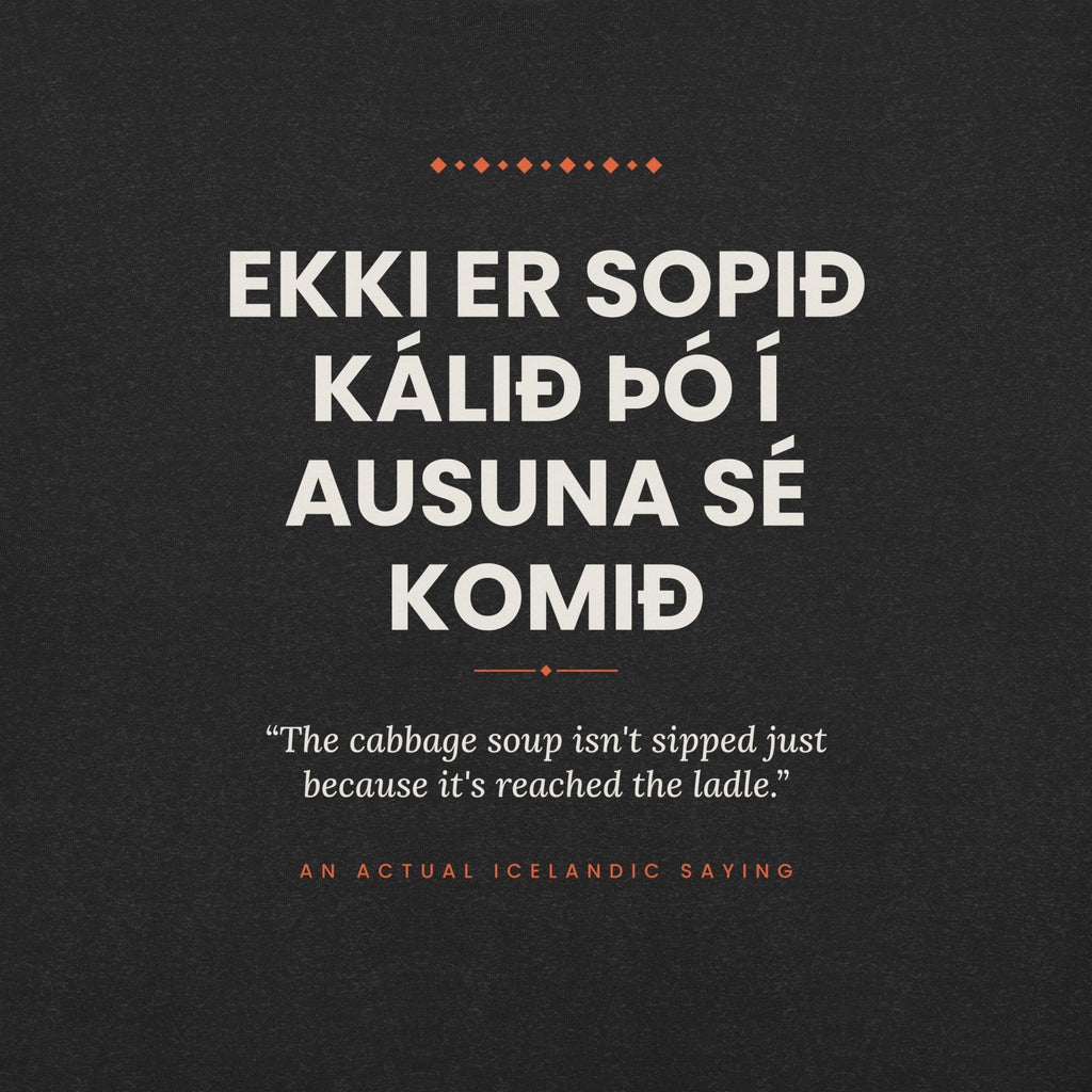 Close-up of the Ekki er sopið kálið þó í ausuna sé komið front print, showing cream lettering, English translation and coral accents on Black Heather fabric.