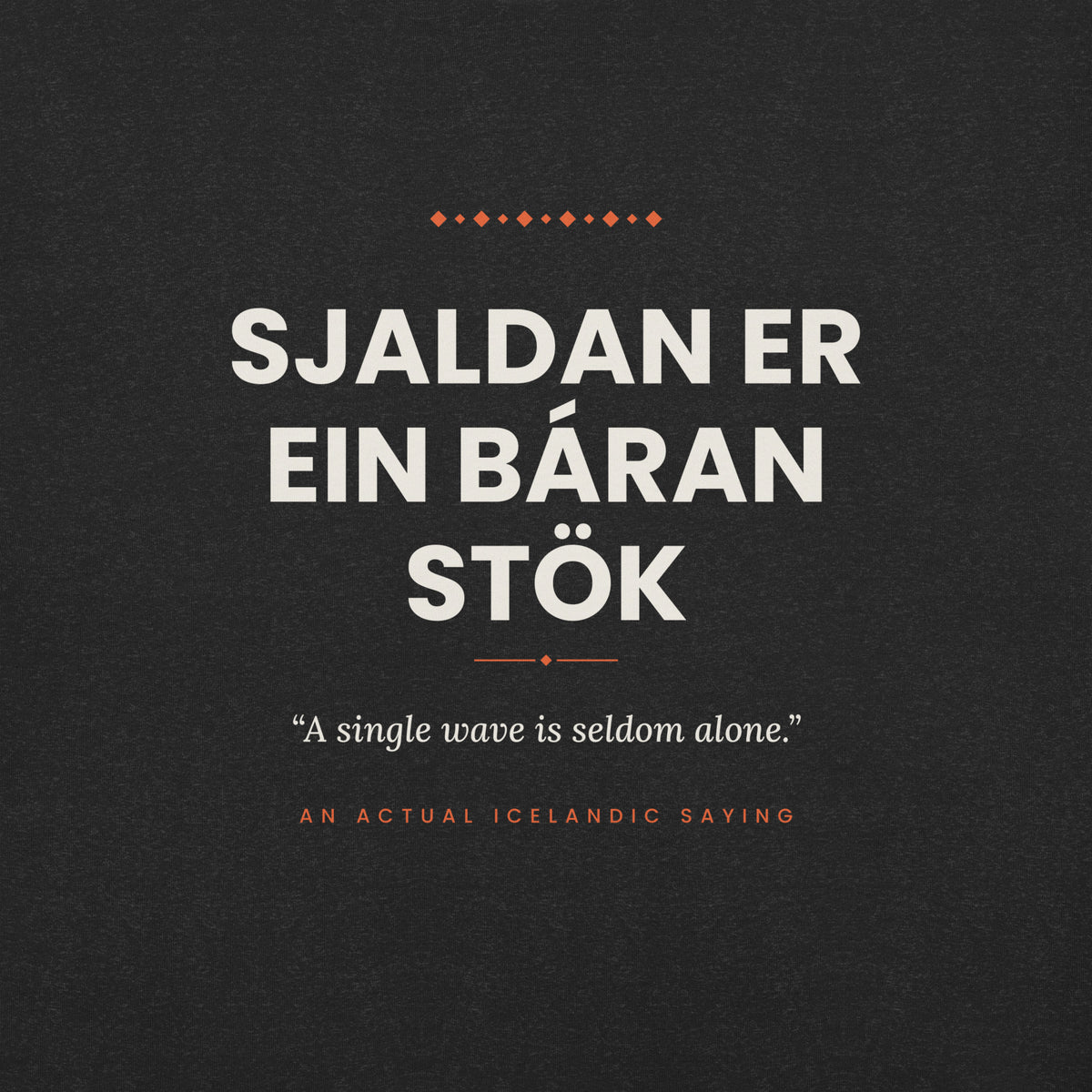 Close-up of the Sjaldan er ein báran stök front print, showing cream lettering, English translation and coral accents on Black Heather fabric.