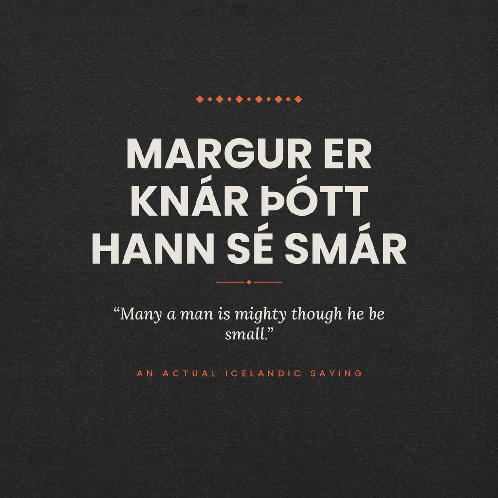 Close-up of the Margur er knár þótt hann sé smár front print, showing cream lettering, English translation and coral accents on Black Heather fabric.