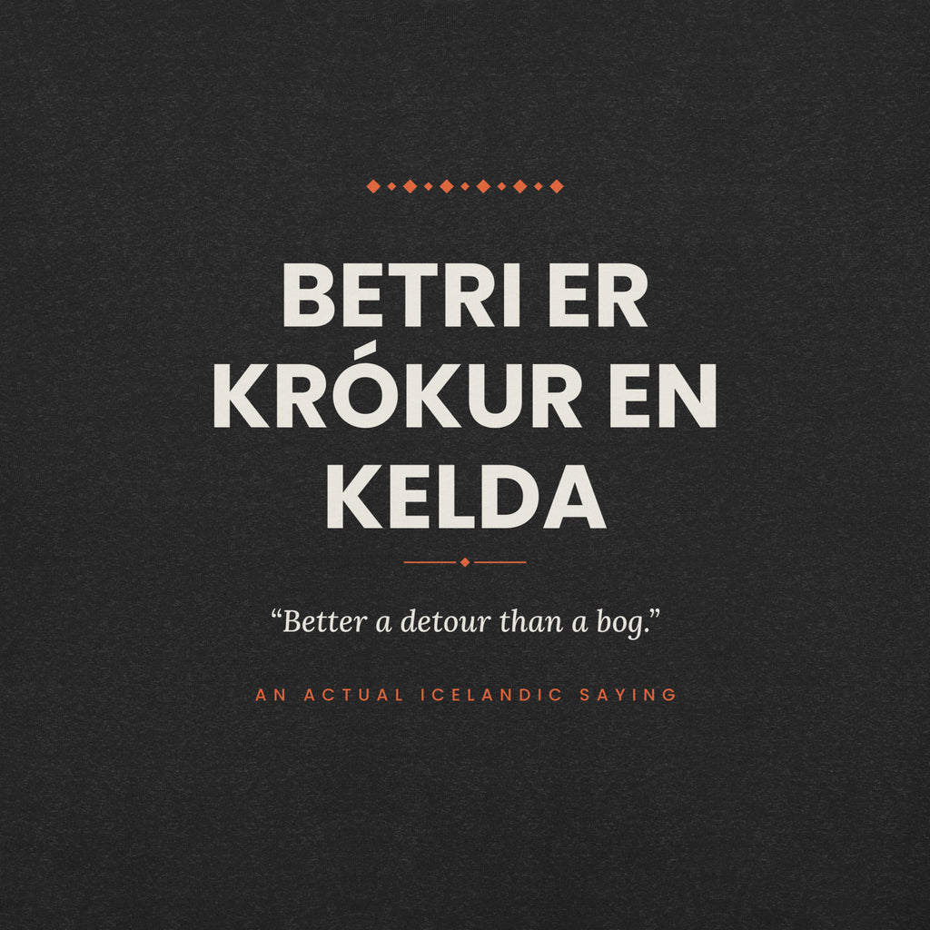 Close-up of the Betri er krókur en kelda front print, showing cream lettering, English translation and coral accents on Black Heather fabric.