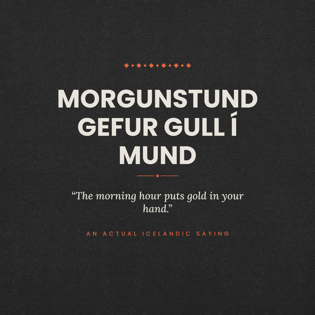 Close-up of the Morgunstund gefur gull í mund front print, showing cream lettering, English translation and coral accents on Black Heather fabric.