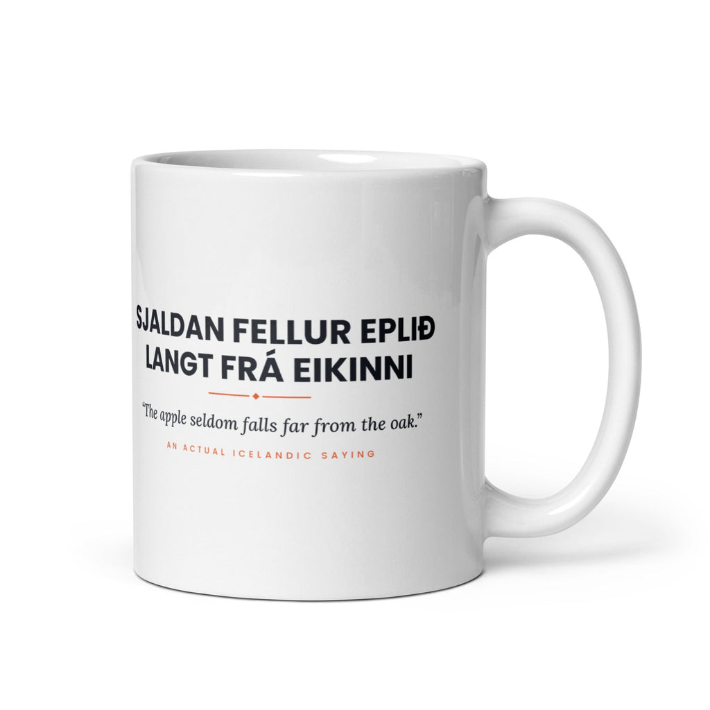 White 11 oz Sjaldan fellur eplið langt frá eikinni mug, handle on the right, showing black lettering, English translation and coral accents.
