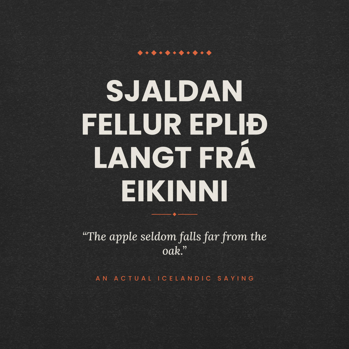 Close-up of the Sjaldan fellur eplið langt frá eikinni front print, showing cream lettering, English translation and coral accents on Black Heather fabric.