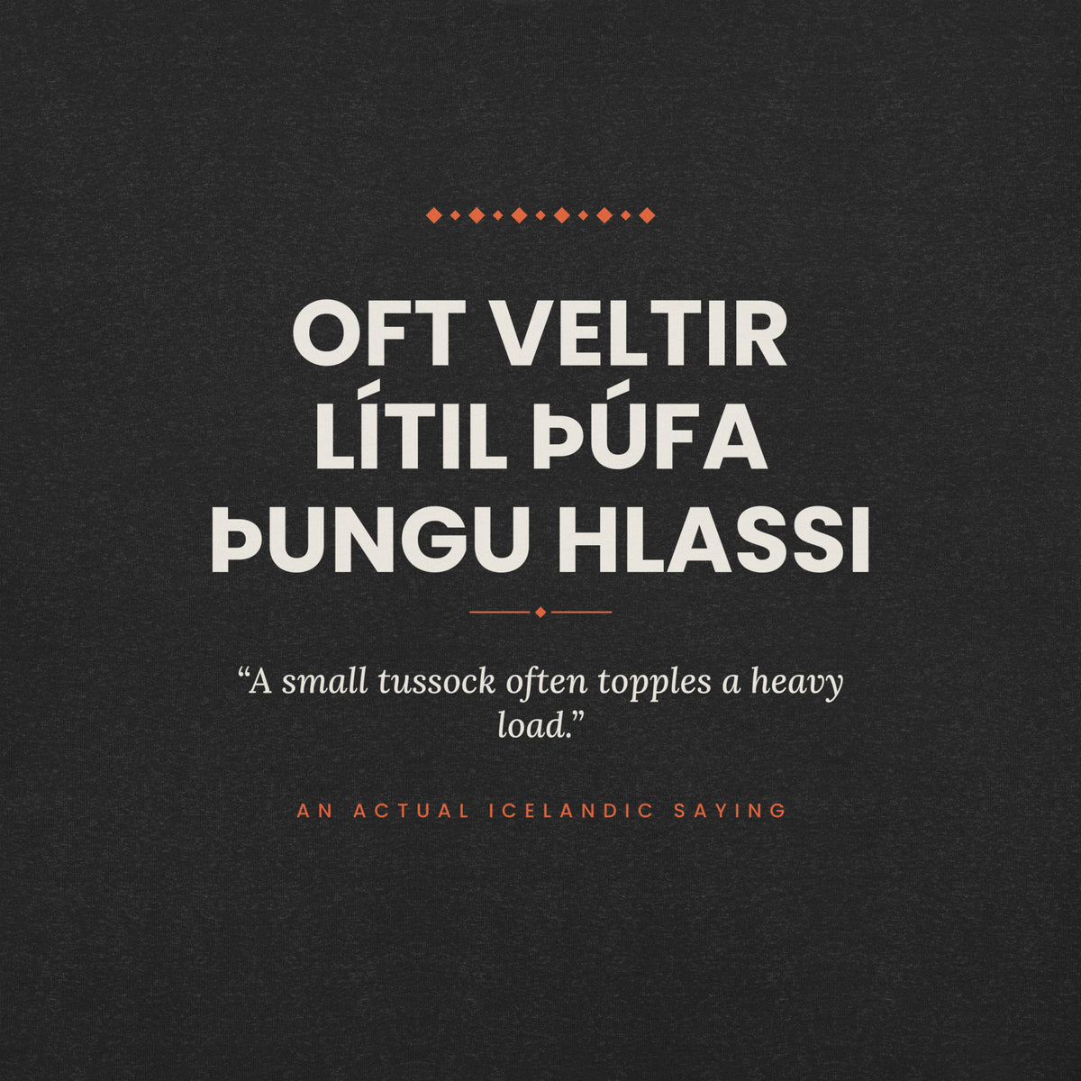 Close-up of the Oft veltir lítil þúfa þungu hlassi front print, showing cream lettering, English translation and coral accents on Black Heather fabric.
