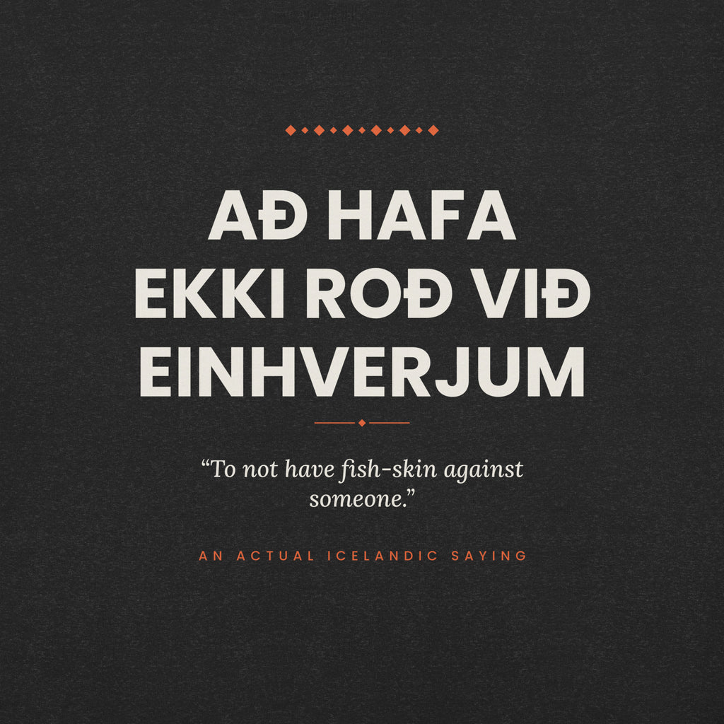 Close-up of the Að hafa ekki roð við einhverjum front print, showing cream lettering, English translation and coral accents on Black Heather fabric.