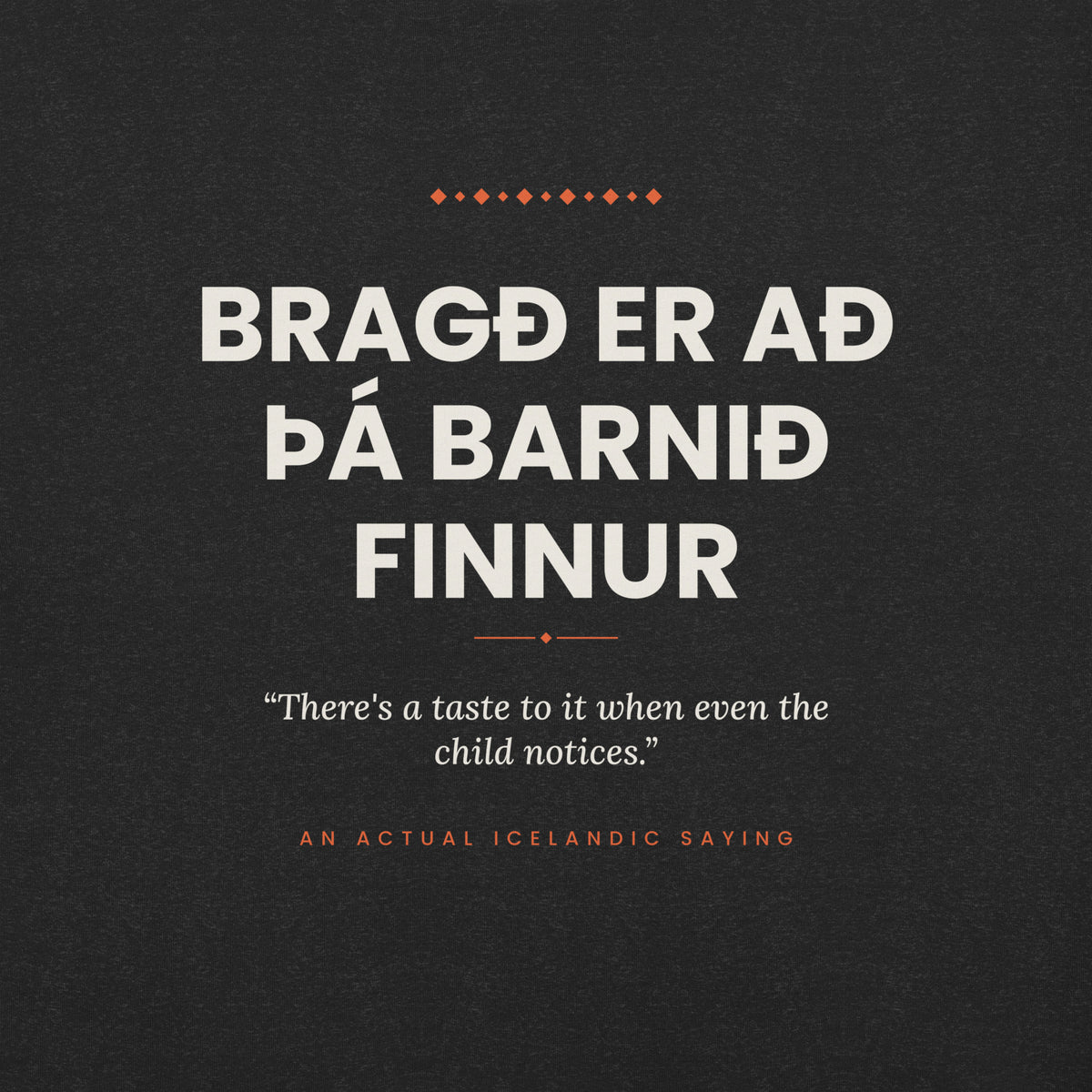 Close-up of the Bragð er að þá barnið finnur front print, showing cream lettering, English translation and coral accents on Black Heather fabric.