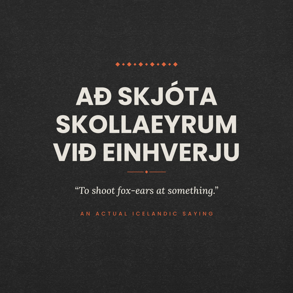 Close-up of the Að skjóta skollaeyrum við einhverju front print, showing cream lettering, English translation and coral accents on Black Heather fabric.