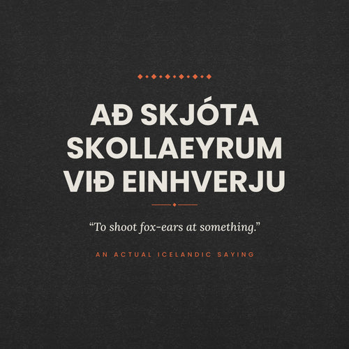 Close-up of the Að skjóta skollaeyrum við einhverju front print, showing cream lettering, English translation and coral accents on Black Heather fabric.