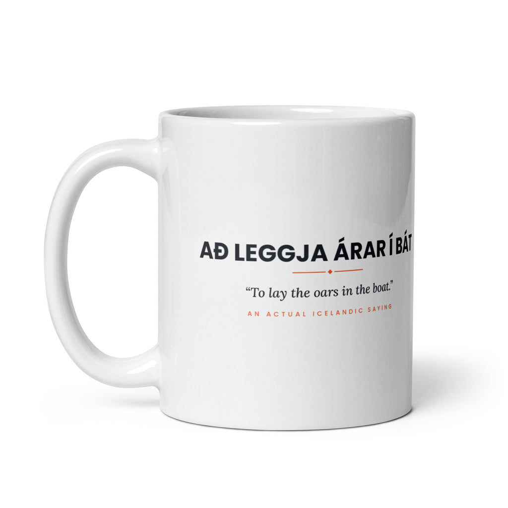 White 11 oz Að leggja árar í bát mug, handle on the left, showing the repeated saying on the other side.