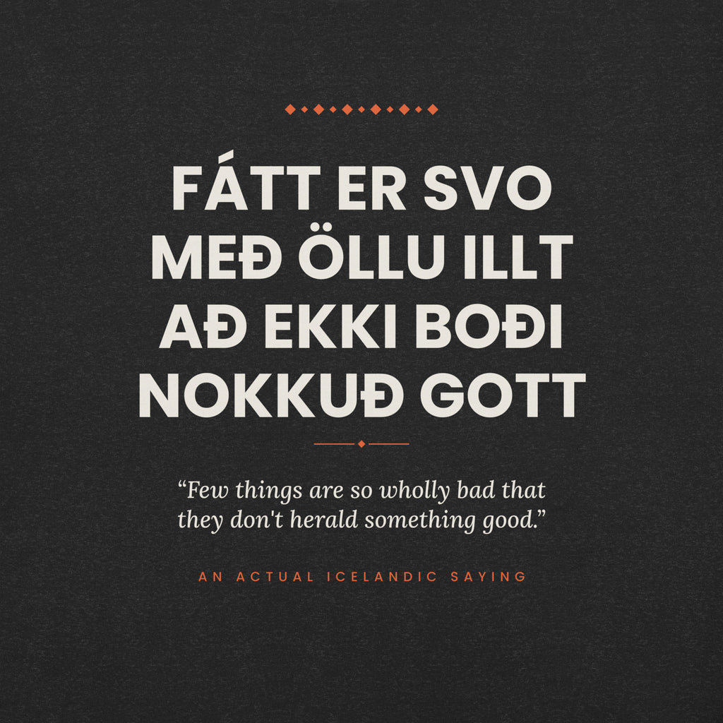 Close-up of the Fátt er svo með öllu illt að ekki boði nokkuð gott front print, showing cream lettering, English translation and coral accents on Black Heather fabric.