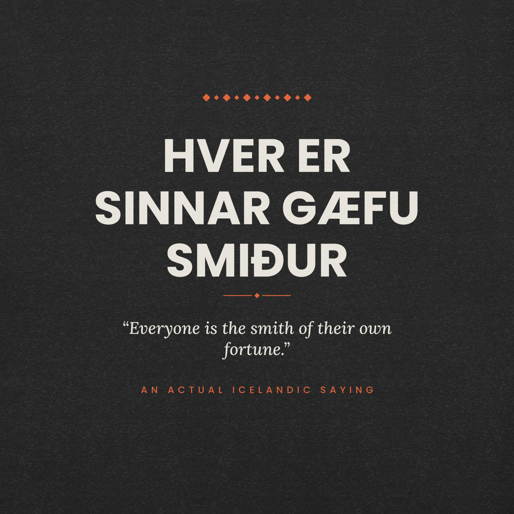 Close-up of the Hver er sinnar gæfu smiður front print, showing cream lettering, English translation and coral accents on Black Heather fabric.