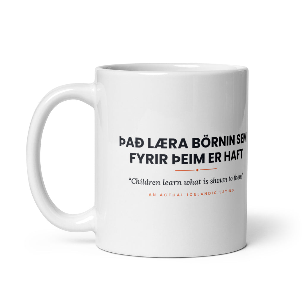 White 11 oz Það læra börnin sem fyrir þeim er haft mug, handle on the left, showing the repeated saying on the other side.