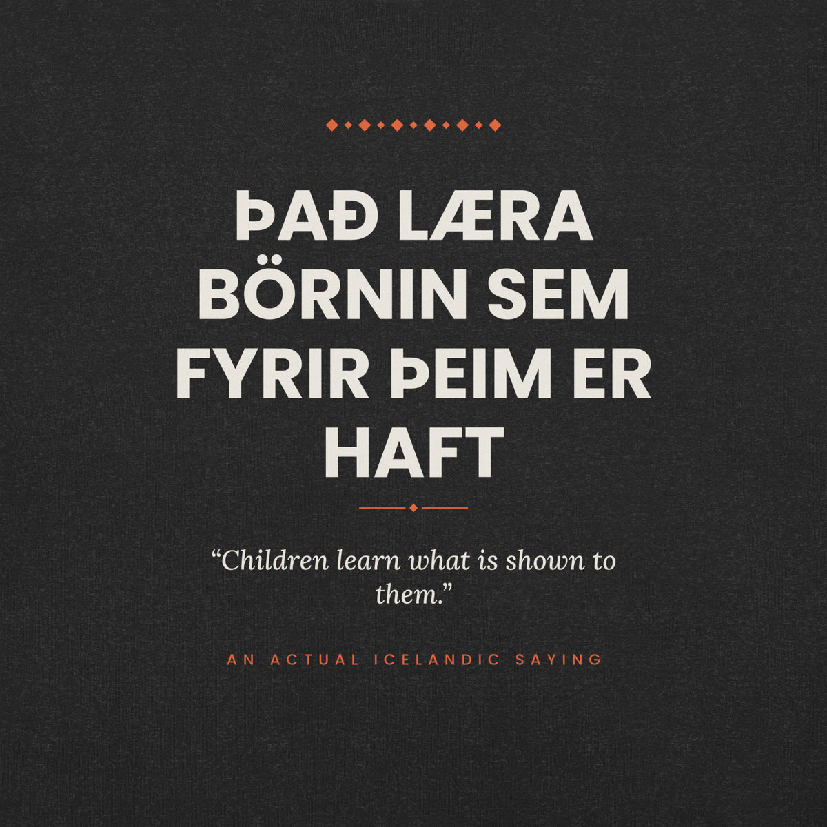 Close-up of the Það læra börnin sem fyrir þeim er haft front print, showing cream lettering, English translation and coral accents on Black Heather fabric.