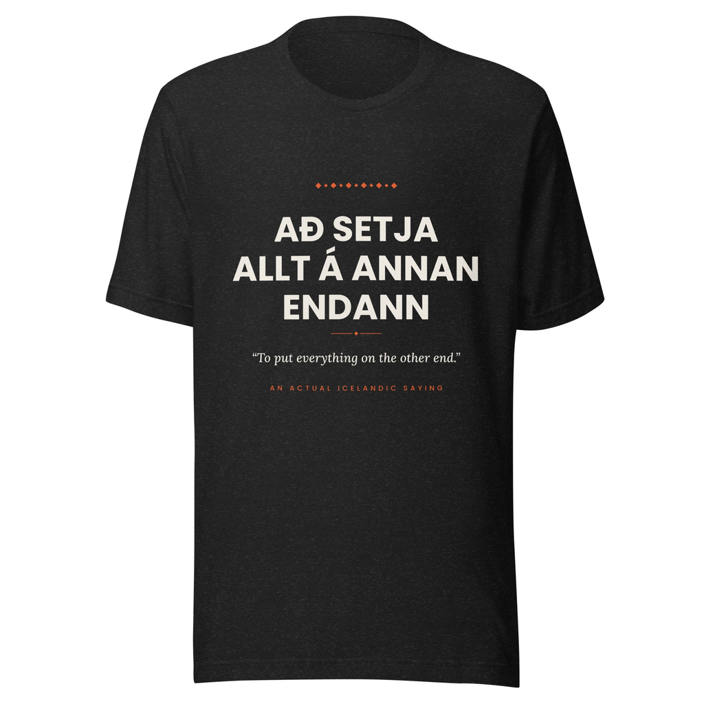 Front view of the Black Heather Að setja allt á annan endann tee, with cream lettering, English translation and coral accents.