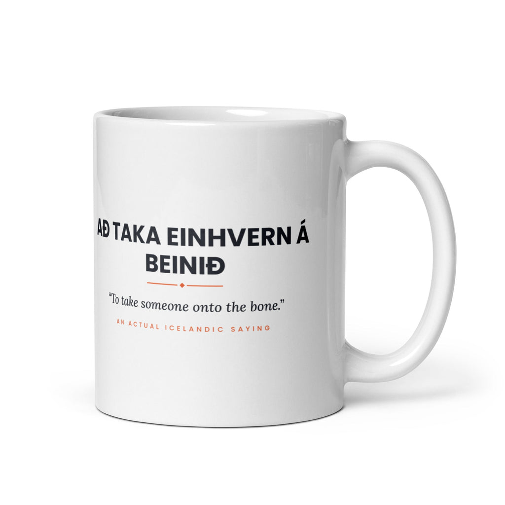 White 11 oz Að taka einhvern á beinið mug, handle on the right, showing black lettering, English translation and coral accents.