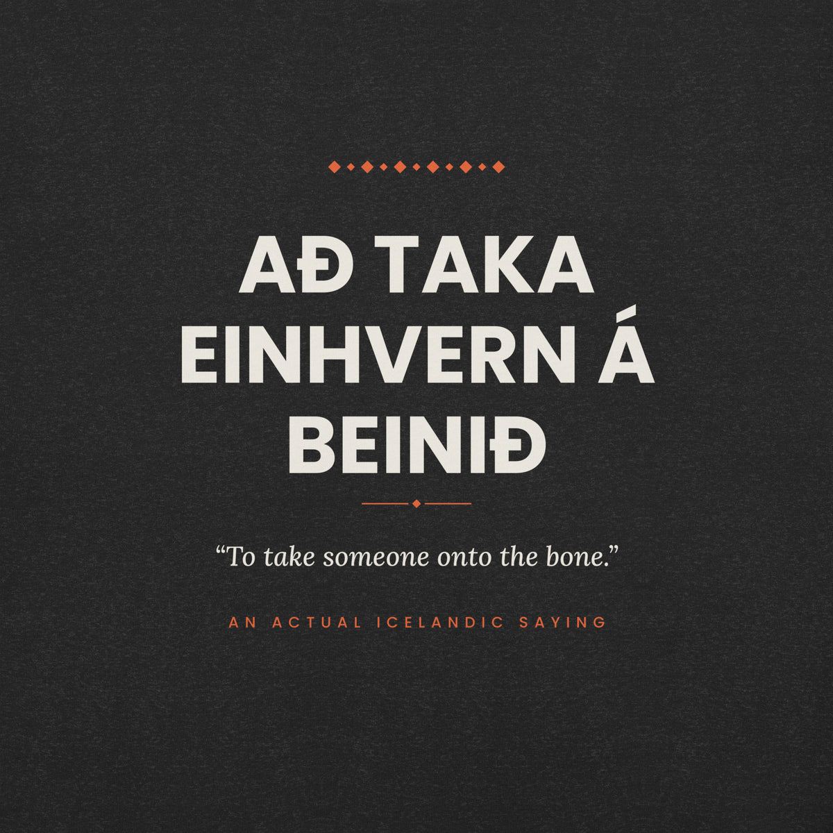 Close-up of the Að taka einhvern á beinið front print, showing cream lettering, English translation and coral accents on Black Heather fabric.