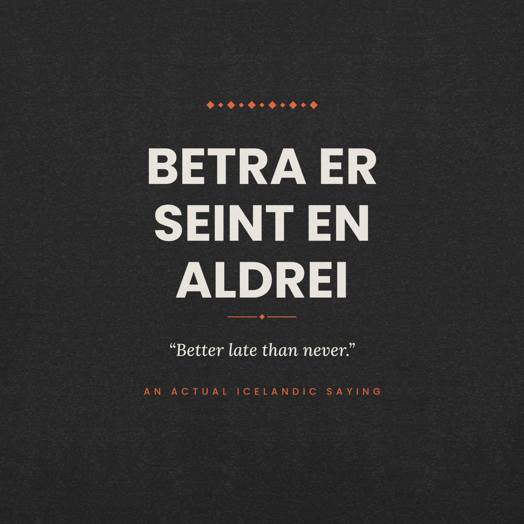 Close-up of the Betra er seint en aldrei front print, showing cream lettering, English translation and coral accents on Black Heather fabric.