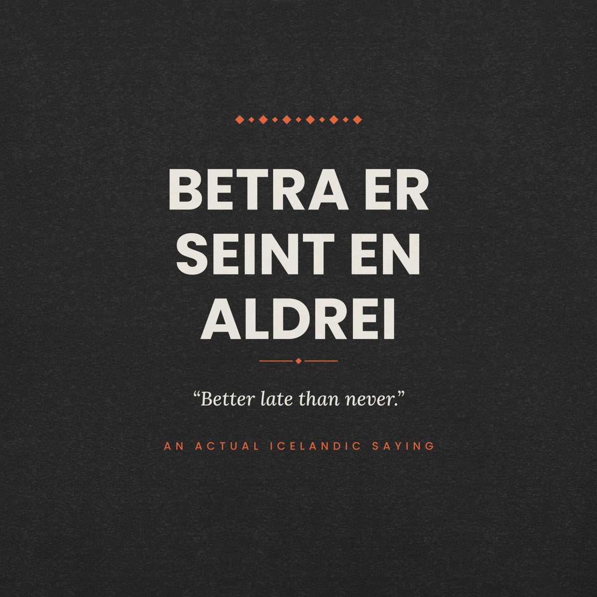 Close-up of the Betra er seint en aldrei front print, showing cream lettering, English translation and coral accents on Black Heather fabric.