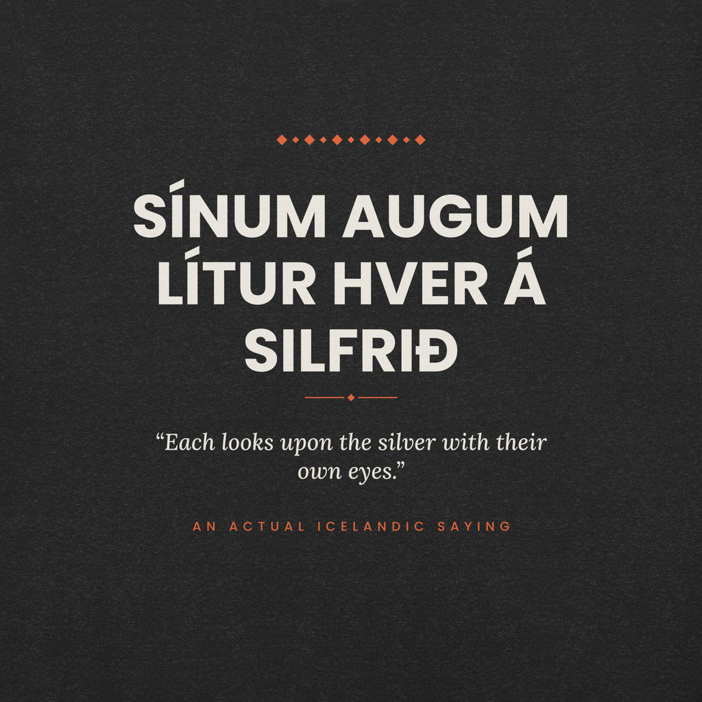 Close-up of the Sínum augum lítur hver á silfrið front print, showing cream lettering, English translation and coral accents on Black Heather fabric.