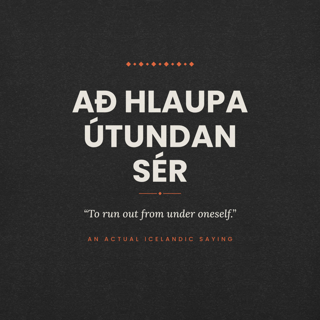 Close-up of the Að hlaupa útundan sér front print, showing cream lettering, English translation and coral accents on Black Heather fabric.