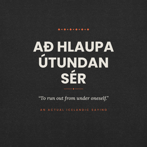 Close-up of the Að hlaupa útundan sér front print, showing cream lettering, English translation and coral accents on Black Heather fabric.