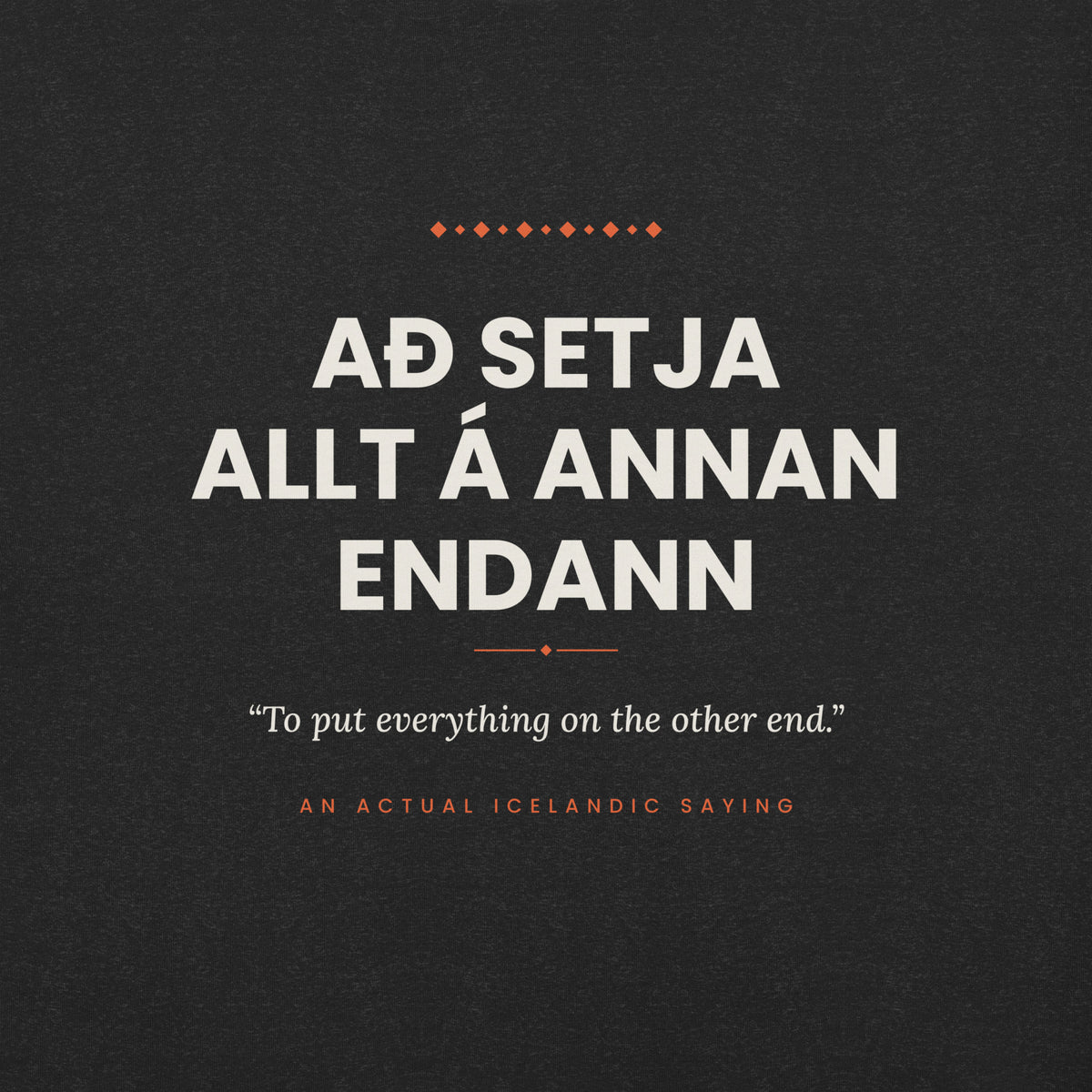 Close-up of the Að setja allt á annan endann front print, showing cream lettering, English translation and coral accents on Black Heather fabric.