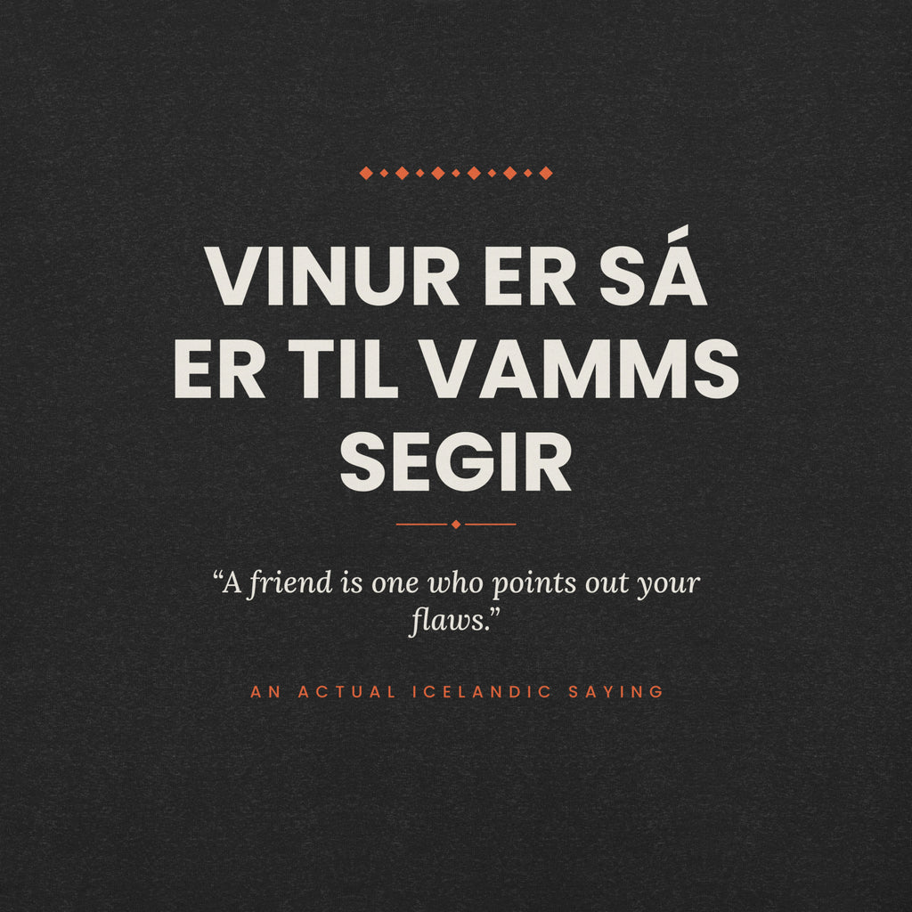 Close-up of the Vinur er sá er til vamms segir front print, showing cream lettering, English translation and coral accents on Black Heather fabric.