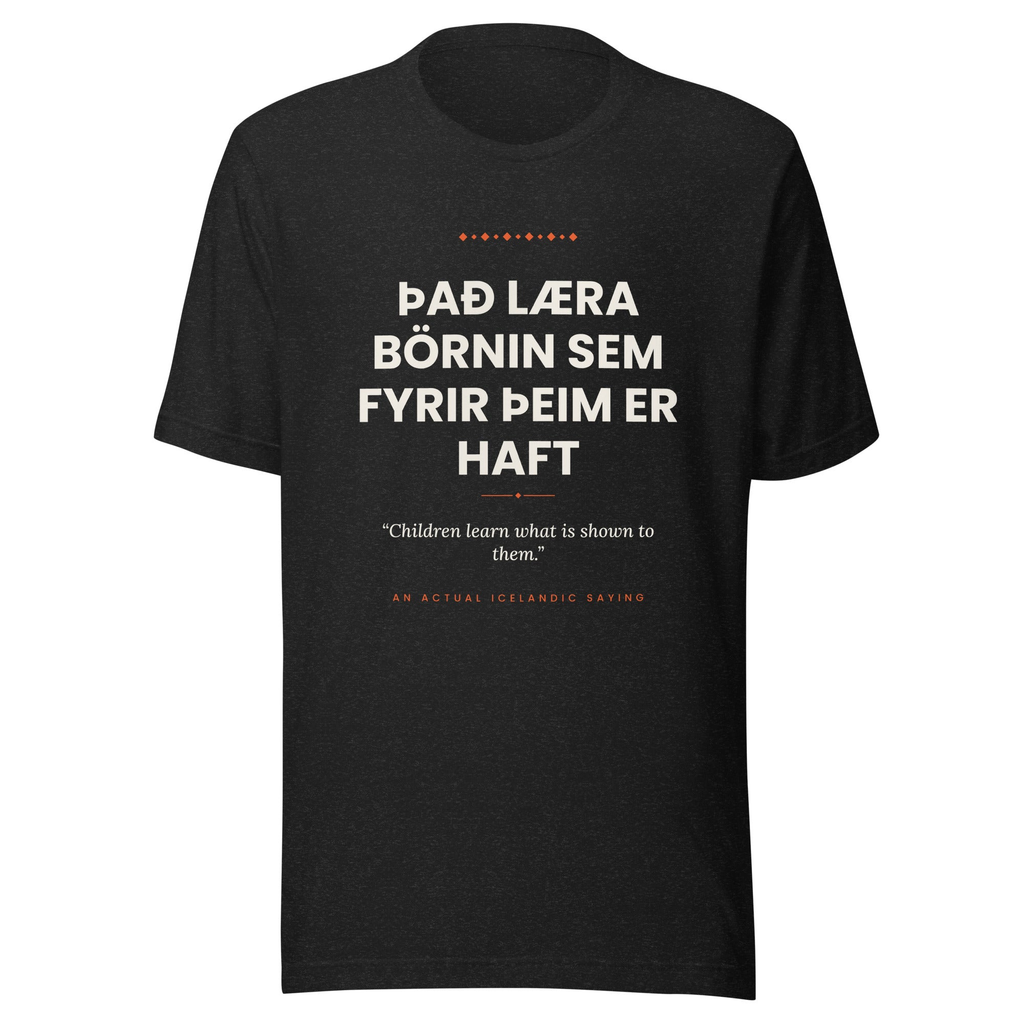 Front view of the Black Heather Það læra börnin sem fyrir þeim er haft tee, with cream lettering, English translation and coral accents.