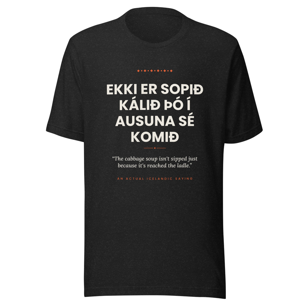 Front view of the Black Heather Ekki er sopið kálið þó í ausuna sé komið tee, with cream lettering, English translation and coral accents.